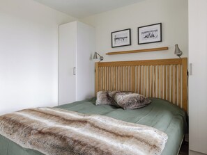 A bedroom with a bed, a wooden headboard, two framed pictures, a bedside lamp, and a fur throw. - Trillevallen 9 by Interhome (Trillevallen)