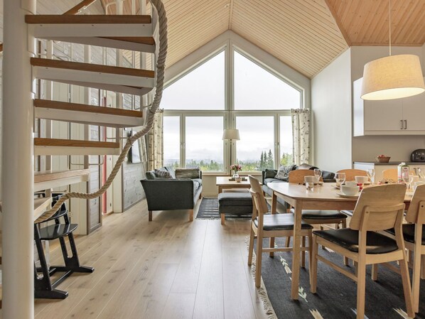 A spacious living area with a high ceiling, a spiral staircase, and large windows offering a view of the outdoors.