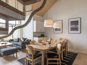Een moderne woonkamer met een eethoek, met een touwschommel, houten balken in het plafond en een groot raam.