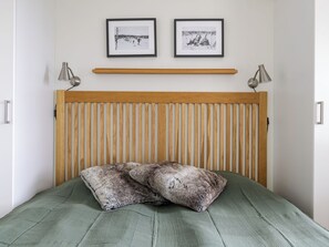 A bedroom with a wooden headboard, two framed pictures, a green bedspread, and two bedside lamps.