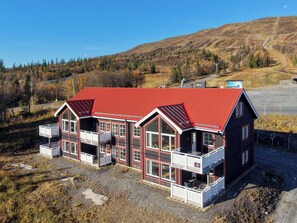 A two-story building with a red roof, multiple balconies, and a view of a mountainous landscape.