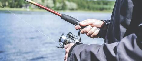 A person holding a fishing rod over a body of water with a forested landscape in the background.