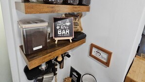 Ein Kaffee-Bereich mit Kaffeesackware, einer Kaffeemühle, einem Schild mit der Aufschrift "The Coffee & Tea Bar" und einem Becherständer.