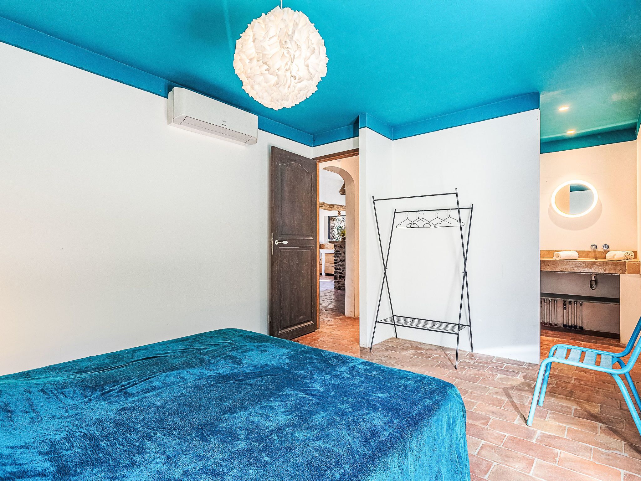 Ein Zimmer mit einem Bett, einem Kleiderhaken, einem Badezimmer mit Waschbecken und Spiegel sowie einer Treppe.