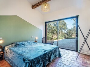 Un dormitorio con cama, una silla, una lámpara y un amplio ventanal corredero que da a un espacio exterior.