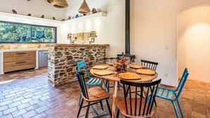 A rustic kitchen with a stone island, wooden chairs, and a dining table set for four. - La Bastide Neuve by Interhome (La Môle)