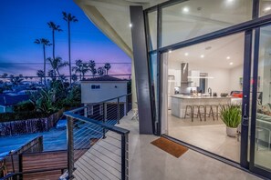 Une cuisine moderne avec une porte vitrée donnant sur un balcon d’où l’on peut admirer des palmiers et un coucher de soleil.