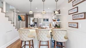 A modern kitchen with a central island, pendant lighting, and a staircase leading to an upper level. - New! Bayfront 3 BD/3BA Retreat with Private Patio! (San Diego)