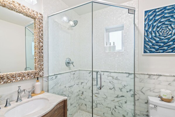 Un baño moderno con ducha de vidrio, paredes de mármol y un espejo grande.