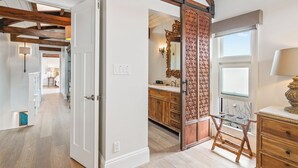 A room with exposed wooden beams, a sliding door with intricate woodwork, a vanity with a mirror, and a window with a view. - New! Bayfront 3 BD/3BA Retreat with Private Patio! (San Diego)