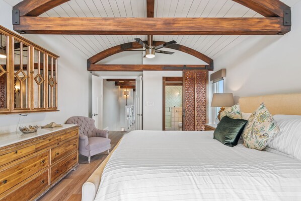 A bedroom with a large bed, wooden headboard, a dresser, a chair, and a ceiling fan. - Bayfront 3 BD/3BA Retreat with Private Patio! (San Diego)