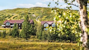 A rural setting with two red-roofed buildings surrounded by greenery and a hill in the background. - Trillevallen 1 by Interhome (Trillevallen)