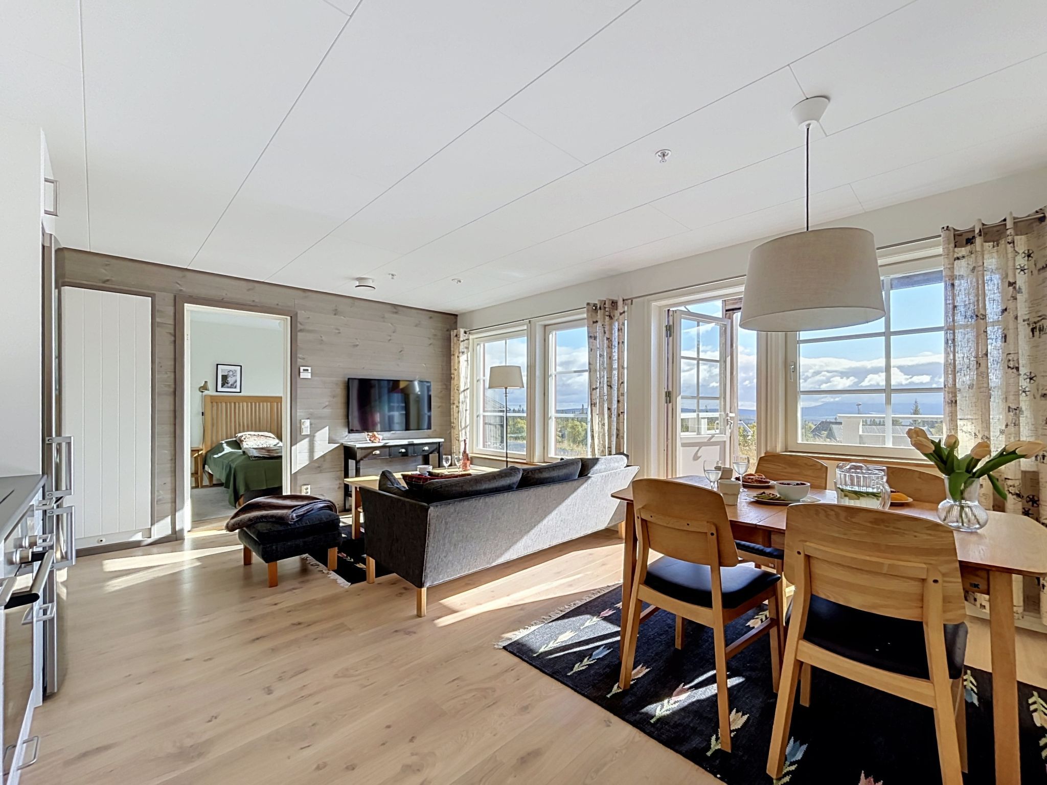 Ett modernt vardagsrum med en soffa, ett matbord och stolar, en tv och stora fönster med utsikt.