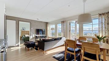 Ett modernt vardagsrum med en soffa, ett matbord och stolar, en tv och stora fönster med utsikt.