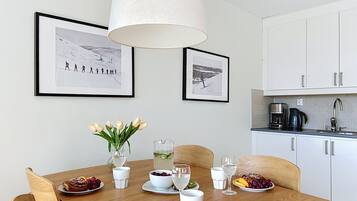 En matplats med ett träbord dukat för en måltid, två inramade fotografier på väggen och ett kök i bakgrunden.