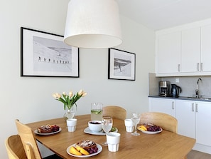 A dining area with a wooden table set for a meal, two framed photographs on the wall, and a kitchen in the background. - Trillevallen 1 by Interhome (Trillevallen)