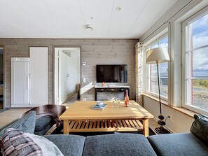 A modern living room with a wooden coffee table, a sofa, a television, and a window with a view. - Trillevallen 1 by Interhome (Trillevallen)