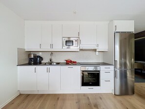 Una cocina moderna con armarios blancos, un refrigerador de acero inoxidable, un microondas, un horno y una cafetera.