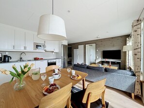 Una cocina moderna con armarios blancos, una mesa de comedor con sillas y una lámpara colgante grande de color blanco.