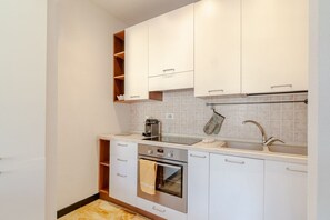 Eine moderne Küche mit weißen Schränken, einem Edelstahlbackofen, einer Spüle und einer gefliesten Rückwand.