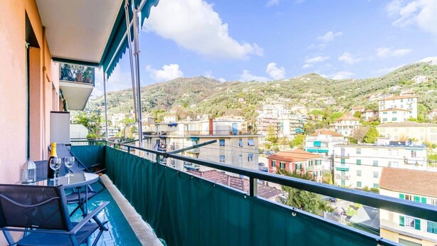A balcony with a table and chairs, overlooking a hillside town. - GuestHost - In Rapallo, a cozy 43 sqm apartment for 3 guests, located on the second floor with an elevator (accessible via steps). Featuring a balcony and reserved parking, a real plus in the city. Rapallo, the heart of the Ligurian Riviera, offers sea,  (Rapallo)