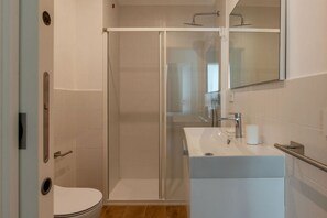A modern bathroom with a glass-enclosed shower, a white sink, and a toilet.