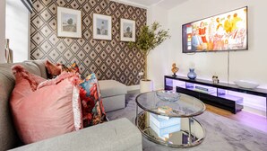 Uma sala de estar moderna com papel de parede estampado, uma televisão de tela plana, uma mesa de centro de vidro e um aparador com objetos decorativos.