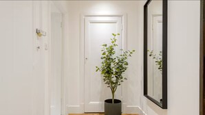 Um corredor com piso de madeira, paredes brancas e um vaso de planta.