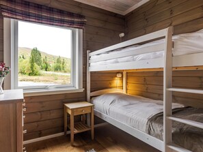 A bunk bed room with a window, a bedside table, and a lamp.