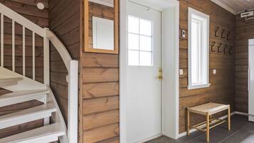 Un intérieur en bois avec un escalier blanc, une porte, un petit banc et un miroir fixé au mur.