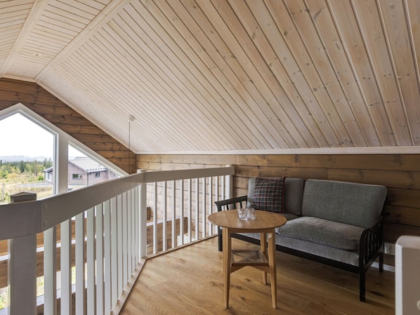 A wooden deck with a railing, a gray sofa, and a round table with glasses.
