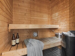 A wooden sauna room with two bottles, a towel, a metal basin, and a large metal container.
