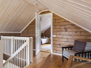 Dormitorio tipo loft con techo de madera, cama, mesita de noche y una silla con cojín a cuadros.