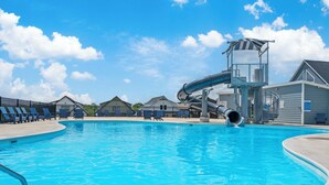 Una piscina con tobogán de agua, sillas de descanso y una torre de salvavidas.