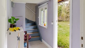 A hallway with a staircase leading to a room, a potted plant, and a window with a view of the outdoors.