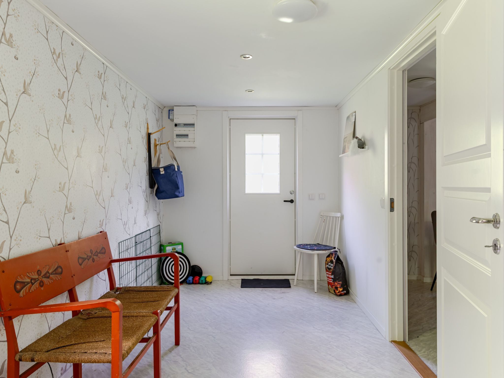 Un pasillo con una puerta blanca, un banco, una silla y una pared con diseño floral.