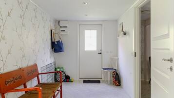 Un pasillo con una puerta blanca, un banco, una silla y una pared con diseño floral.