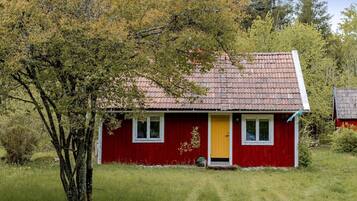 A red house with a yellow door, surrounded by grass and trees.