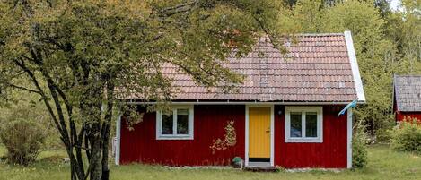 A red house with a yellow door, surrounded by grass and trees.