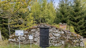 A stone structure with a black door, surrounded by trees and a grassy area.