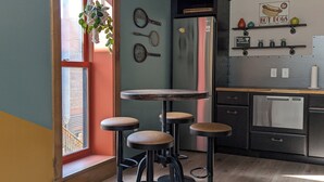 Une cuisine avec une table ronde et des tabourets, un réfrigérateur et une fenêtre donnant sur des immeubles.