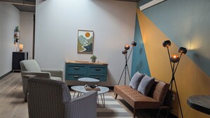 Un salon moderne avec un canapé, des fauteuils, une table basse et un meuble. Il y a un tableau au mur et une lampe sur pied.