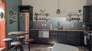 Une cuisine moderne dotée d’un îlot central, de tabourets de bar, d’un réfrigérateur, d’un lave-vaisselle et d’un coin repas agrémenté d’une enseigne indiquant « DINER ».