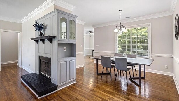 A dining area with a gray built-in fireplace, a dining table with chairs, and a large window with blinds.