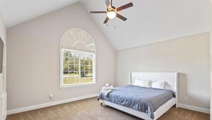 A bedroom with a sloped ceiling, a ceiling fan, a large window with a view, and a bed with a white headboard.