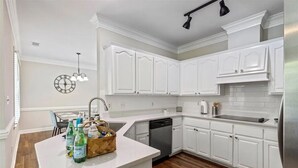 A kitchen with white cabinetry, a wooden countertop, a built-in dishwasher, and a clock on the wall.