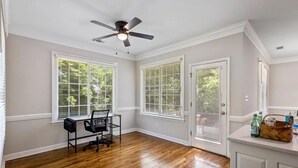 A spacious room with hardwood flooring, a ceiling fan, and large windows with blinds.