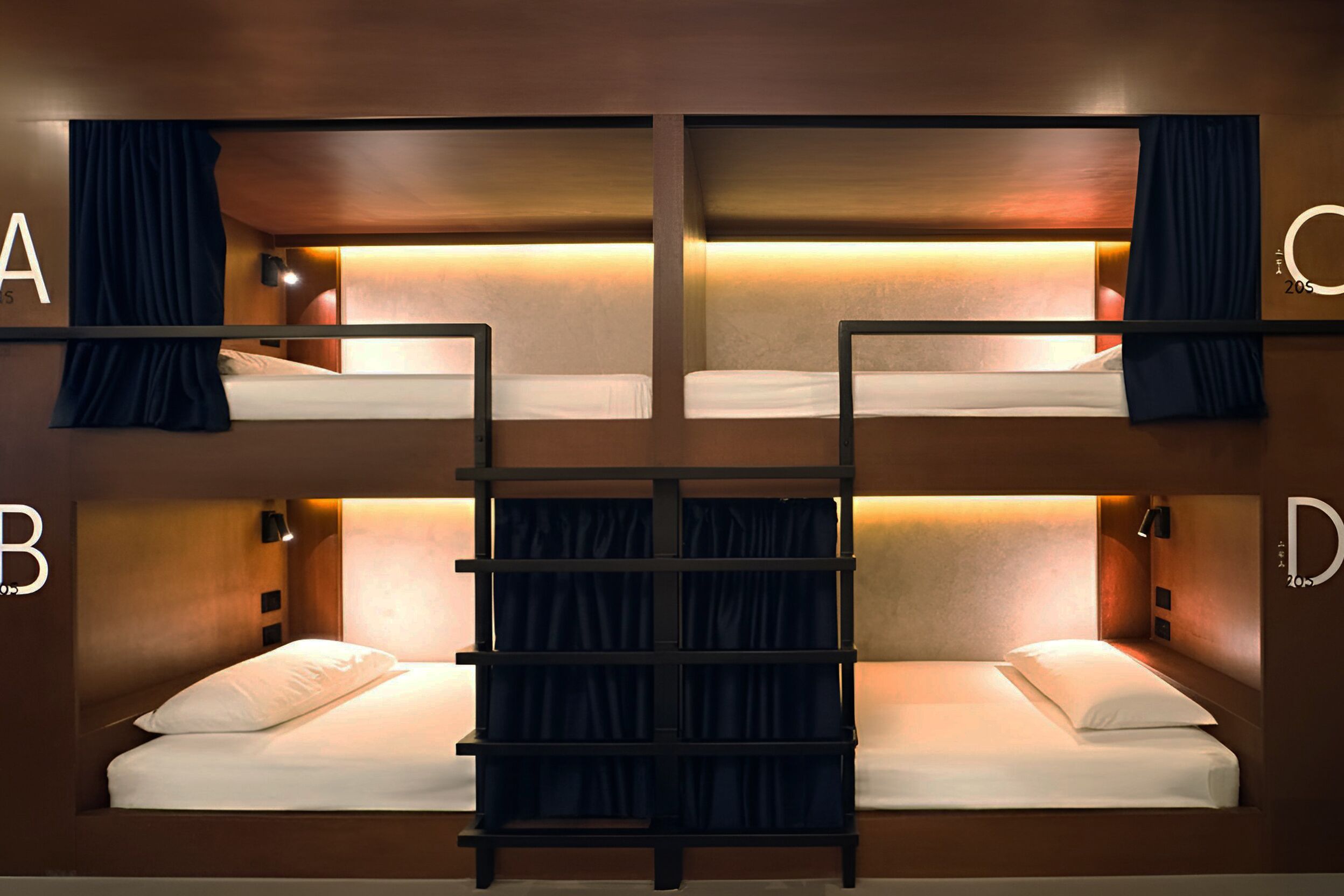 Habitación con literas, una escalera, dos mesitas de noche y una lámpara fijada a la pared.