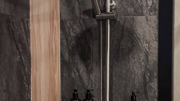 A modern shower with a rain showerhead and handheld showerhead, mounted on a wall with dark marble tiles.