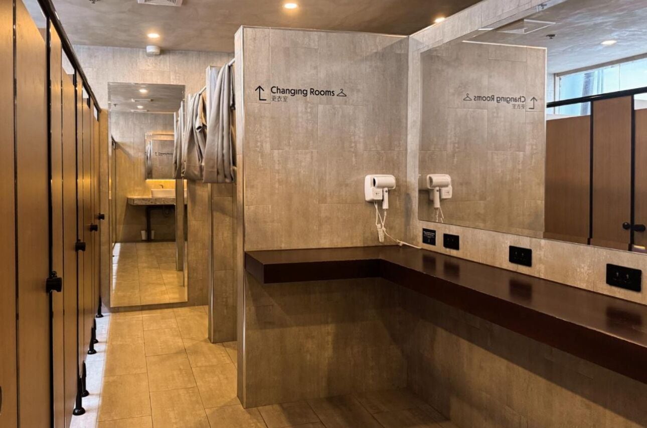 Un baño de hotel moderno con vestuarios, secamanos y un largo pasillo.